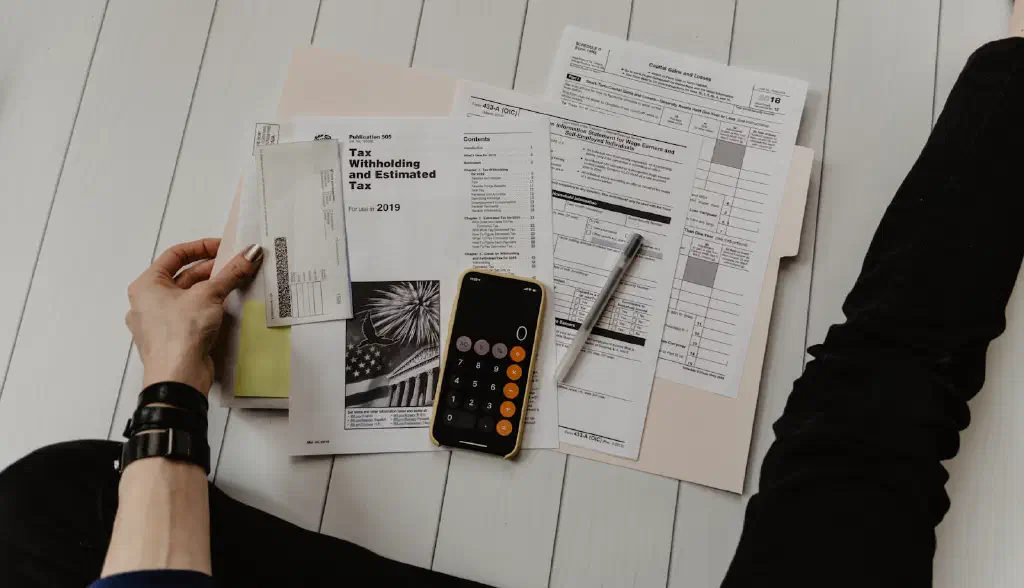A financial analyst reviewing contract documents and spreadsheets on a laptop